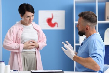 Gastroenterologist consulting patient with stomach pain in clinic, selective focus