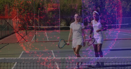 Walking two tennis players in white dresses chatting and smiling on outdoor hard court with rackets