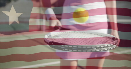 Balancing female tennis player holding racket on outdoor tennis court, with ball hovering above
