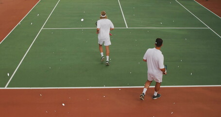 Walking tennis players practicing on green hard court, with rackets white lines net headband