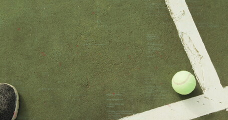 Tennis ball resting in corner of green court near white lines, with athletic sneaker, copy space