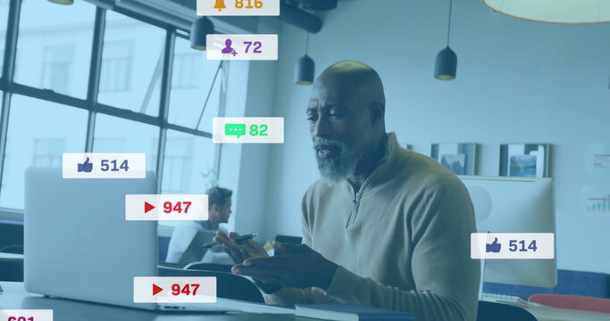 Bearded man analyzing social media icons on smartphone and laptop in open-plan office with stylus - Powered by Adobe