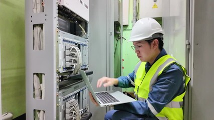 Network technician inspection on server rack cables using laptop in data center wearing safety helmet and reflective vest ensuring data center safety and efficient network maintenance - Powered by Adobe