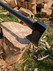 black metal axe in a wooden stump against a background of grass and logs