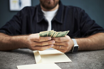 Anonymous Caucasian man counting cash at desk in bank office, holding stack of dollar bills with...