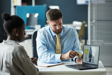 Caucasian male bank assistant explaining financial document on laptop to Black young woman in...