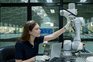 female robotics trainee adjusting robotic arm in smart factory using laptop and manual control...