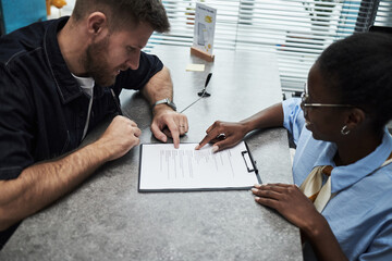 Caucasian young adult man discussing document with Black young female bank worker at office...