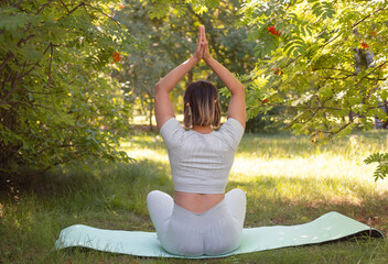 Woman practices yoga outdoors in lotus position and meditates in green park. Concept of healthy...