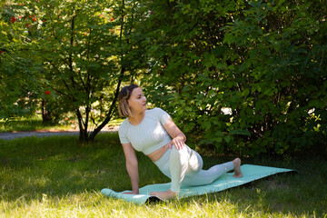 Woman in white tracksuit takes yoga pose on park mat. Woman smiles and stretches her arms and legs....