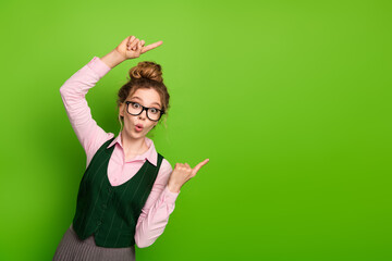 Young woman pointing up and to the side while standing against a bright green background wearing...