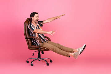 Fototapeta premium Excited young man enjoying a playful moment on an office chair against a vibrant pink background