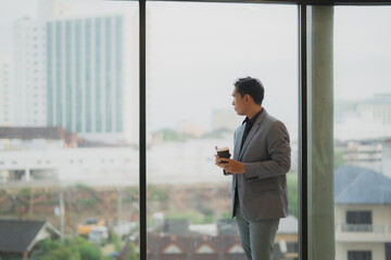 Pensive businessman sipping coffee while gazing out the window on a rainy day, reflecting on the...