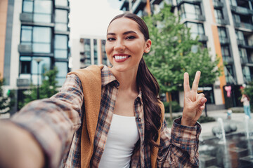 Smiling young woman taking a selfie in an urban park during a sunny day for a casual and stylish...