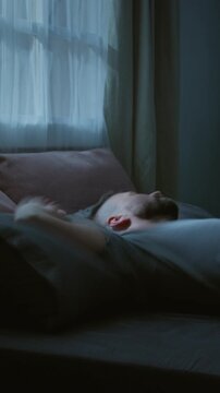 Vertical time lapse of young Caucasian man suffering from PTSD turning and squirming in bed at night, experiencing violent nightmare, suffering from sleep deprivation