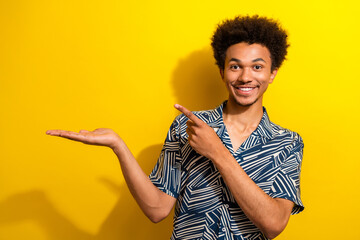 Smiling young man gesturing with open hand in front of bright yellow background showcasing cheerful...