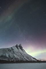 Dancing green and purple aurora borealis light up the starry sky over Norway majestic Otertinden,...
