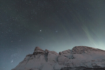 Dancing green and purple aurora borealis light up the starry sky over Norway majestic Lyngen Alps,...