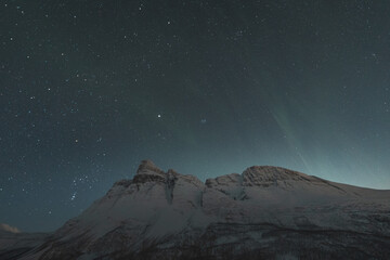 Dancing green and purple aurora borealis light up the starry sky over Norway majestic Otertinden,...