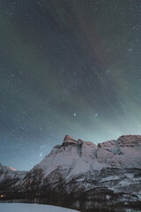 Dancing green and purple aurora borealis light up the starry sky over Norway majestic Otertinden,...