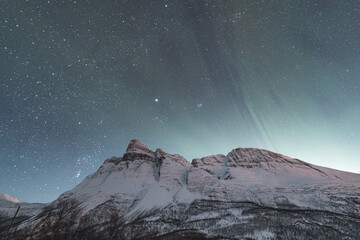 Dancing green and purple aurora borealis light up the starry sky over Norway majestic Lyngen Alps,...