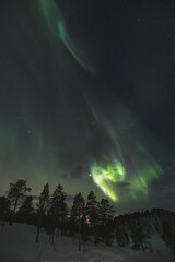 Strong explosion of green aurora borealis sweep across a star-speckled Arctic sky, painting the...