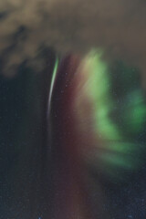 Waves of vivid green and red aurora borealis sweep across a star-speckled Arctic sky, painting the...