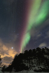 Waves of vivid green and red aurora borealis sweep across a star-speckled Arctic sky, painting the...