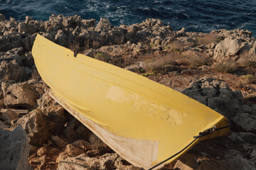 Old yellow canoe fragment on rocky seashore with blue sea in background