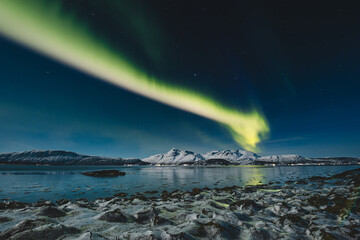 Aurora Borealis glows above Norway Malangen Fjord in Troms, painting the starry night with green...