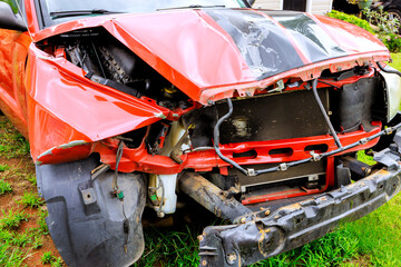 Damaged red pickup truck with severe front end collision in rural setting during daytime
