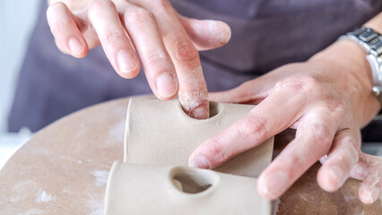 A close-up shot of a middle-aged woman artist shaping clay with sculpting tools at a table in an...