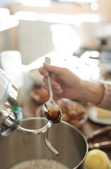 A baker lovingly adds a spoonful of golden honey to a mixer bowl filled with dough, preparing to bake traditional Romanian Mucenici in a cozy kitchen setting