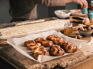 Freshly baked Mucenici rest on parchment paper atop a rustic wooden table. In the background, a...