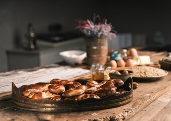 Delicious, fresh baked Mucenici sit in a wooden tray on a rustic table in a kitchen. Ingredients,...