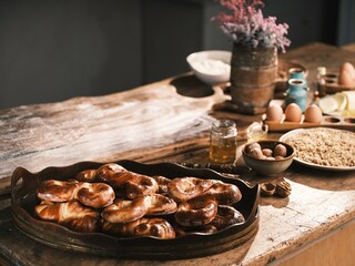 On a wooden table, freshly baked Mucenici sit on a tray, surrounded by ingredients like honey, eggs, and walnuts, ready to enjoy as a spring treat
