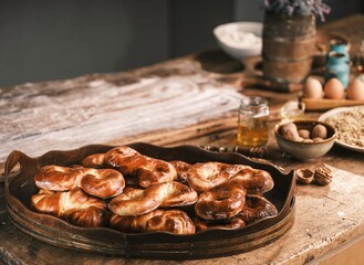 Warm and delicious Mucenici pastries, fresh from the oven, grace a wooden tray. Baking ingredients, eggs, flour and walnuts are arranged on the rustic table in preparation
