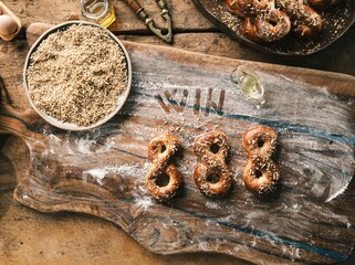 Freshly baked Mucenici, shaped like eights, are displayed on a flour-dusted wooden board,...