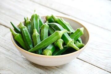 Close-up of fresh okra in a bowl on rustic wooden surface.