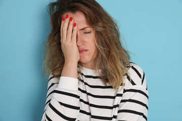 Woman suffering from hangover on light blue background