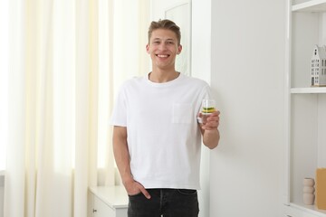 Smiling man with glass of water with cucumber and lemon near white wall indoors. Refreshing drink