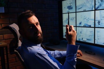 Security guard monitoring CCTV cameras and using walkie talkie in office at night