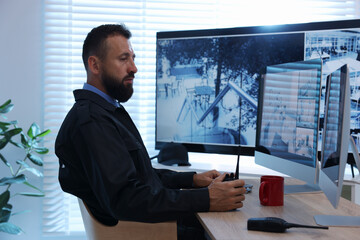 Security guard with walkie talkie monitoring CCTV cameras in office
