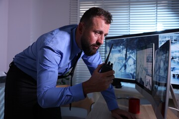 Security guard monitoring CCTV cameras and using walkie talkie in office