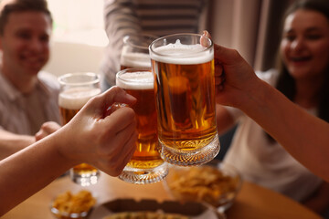 Group of happy friends clinking glasses of beer at table indoors, selective focus