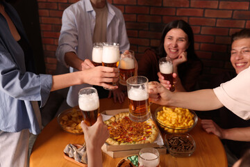 Group of happy friends clinking glasses of beer at table indoors, selective focus