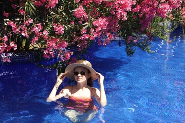 Girl with straw hat in swimming pool outdoors on sunny day, space for text