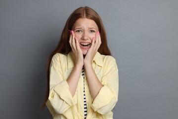 Teenage girl suffering from panic attack on grey background