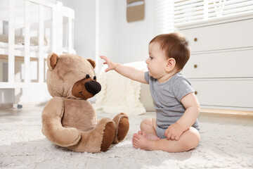 Cute little baby playing with teddy bear in room