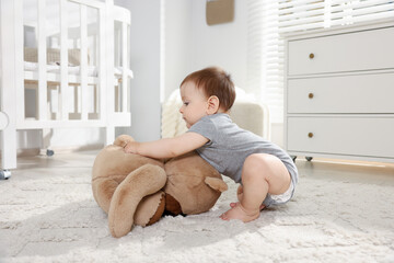 Cute little baby playing with teddy bear in room
